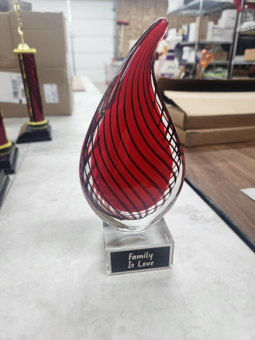 Red glass teardrop award with 'Family Is Love' inscription on a table in a workshop.