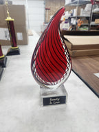 Red glass teardrop award with 'Family Is Love' inscription on a table in a workshop.