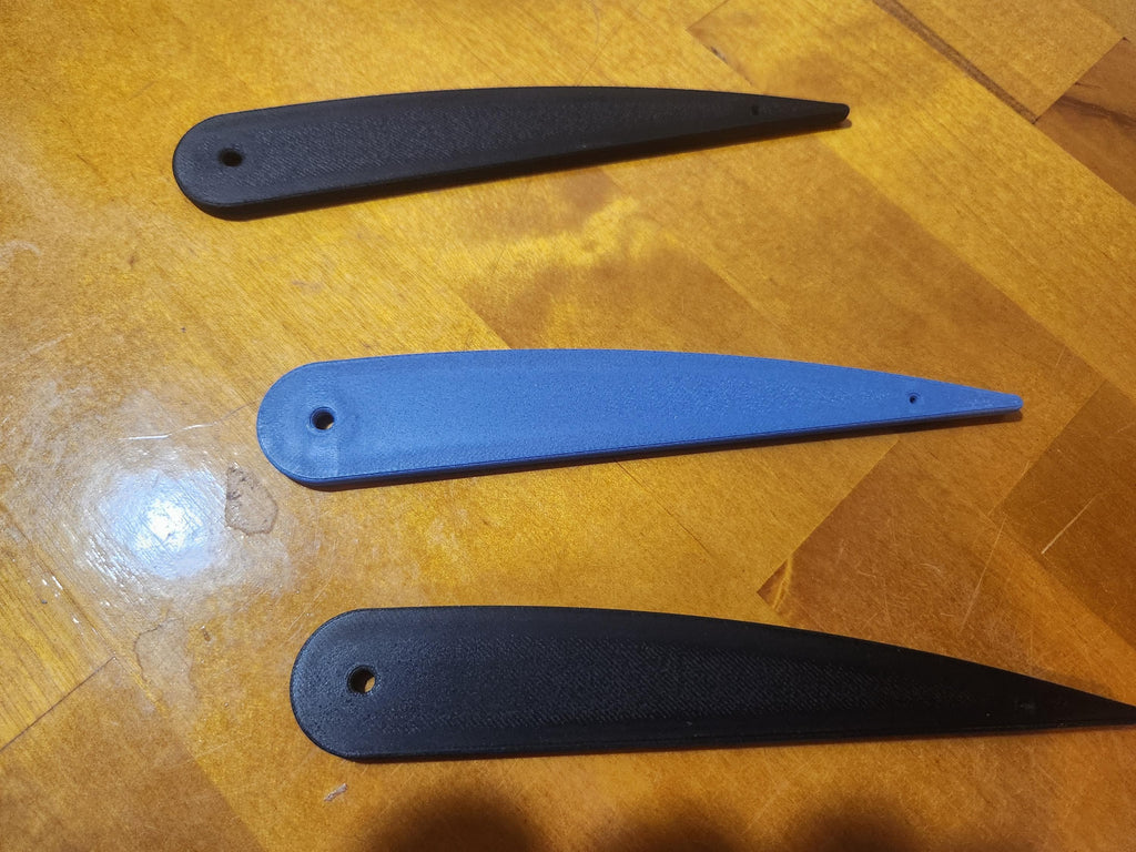 Three 3D printed plastic fan blades, two black and one blue, on a wooden surface.