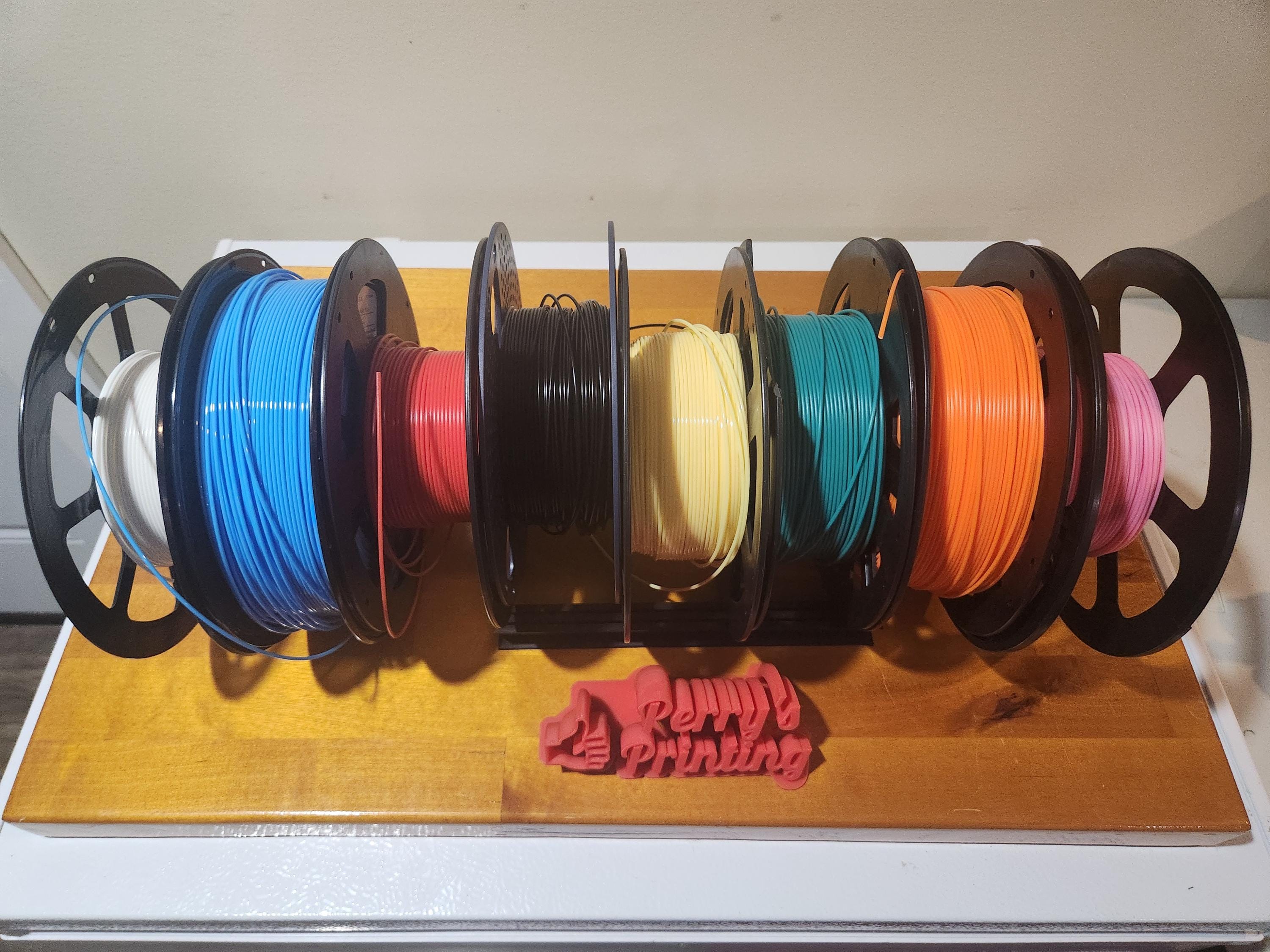 Multiple colorful 3D printer filament spools on a wooden stand, organized for printing projects