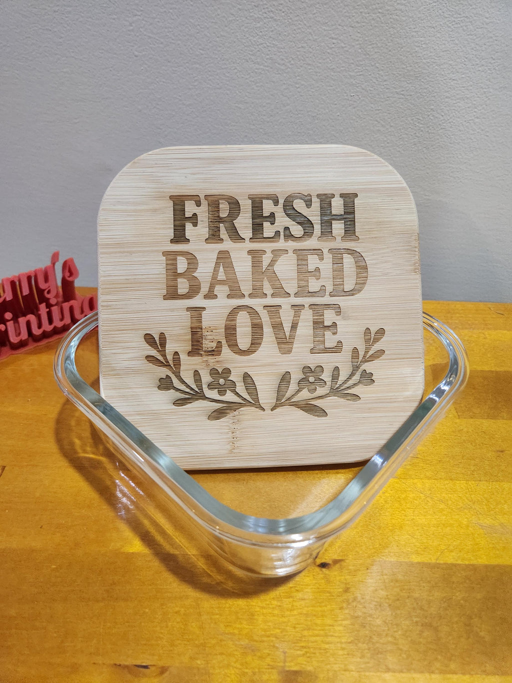 Laser engraved bamboo lid with 'Fresh Baked Love' and floral design on a glass container.
