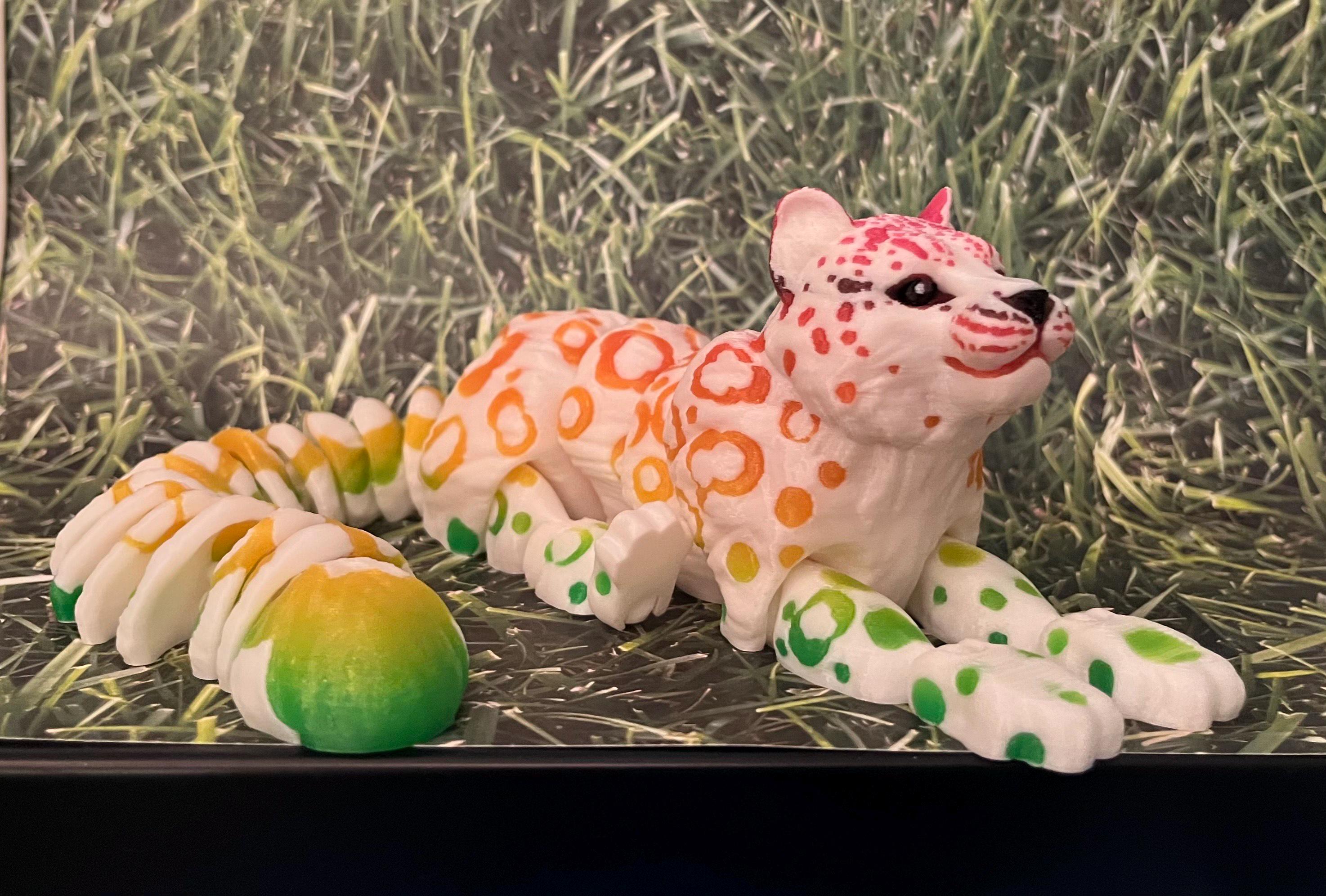 Colorful 3D printed fantasy cat figurine with orange, green, and pink spots on grass background