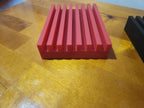 Red 3D printed slotted organizer block on wooden surface, desktop accessory