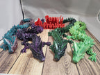 Colorful 3D printed articulated dragon figures on wood surface, Perry's Printing sign in background.