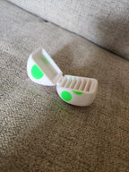 3D printed white case with green spots, open on a beige fabric surface
