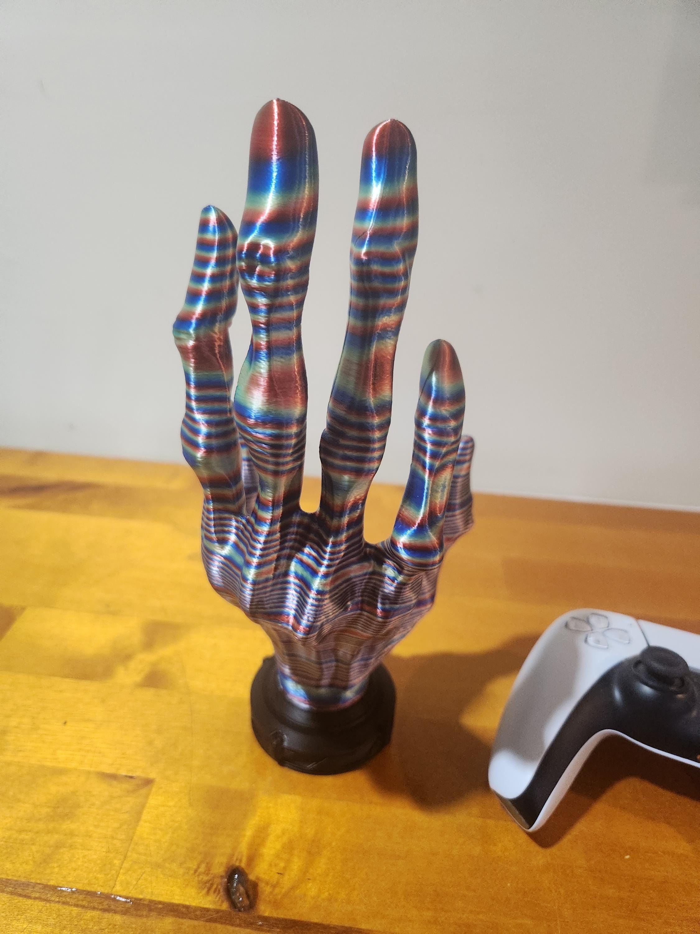 Colorful 3D printed skeleton hand on a wooden surface beside a gaming controller
