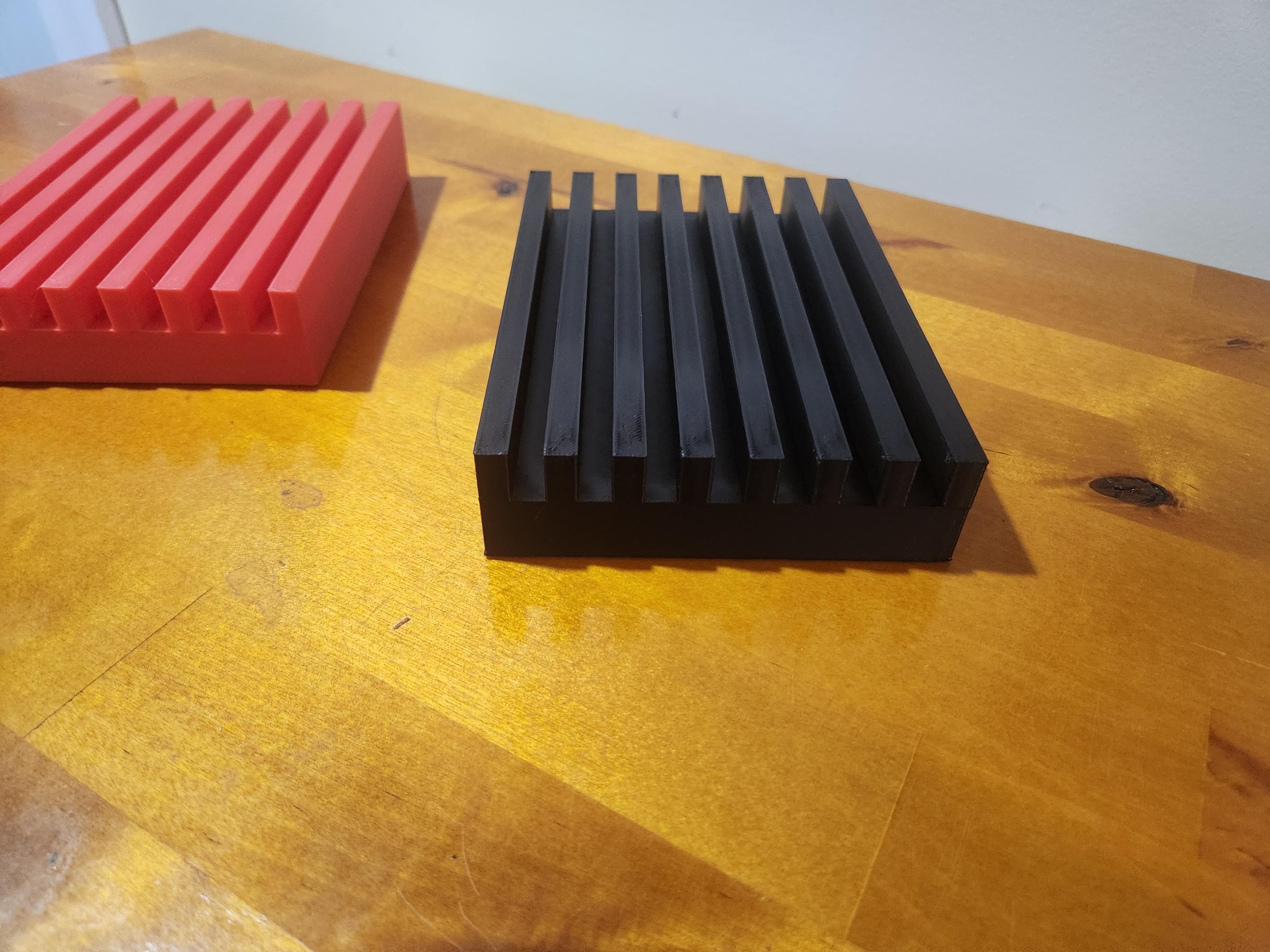 Black and red 3D printed slotted blocks on a wooden table, used for organizing or display.
