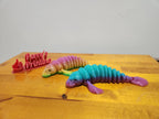 Two rainbow-colored 3D printed articulated sea creatures on a wooden surface.