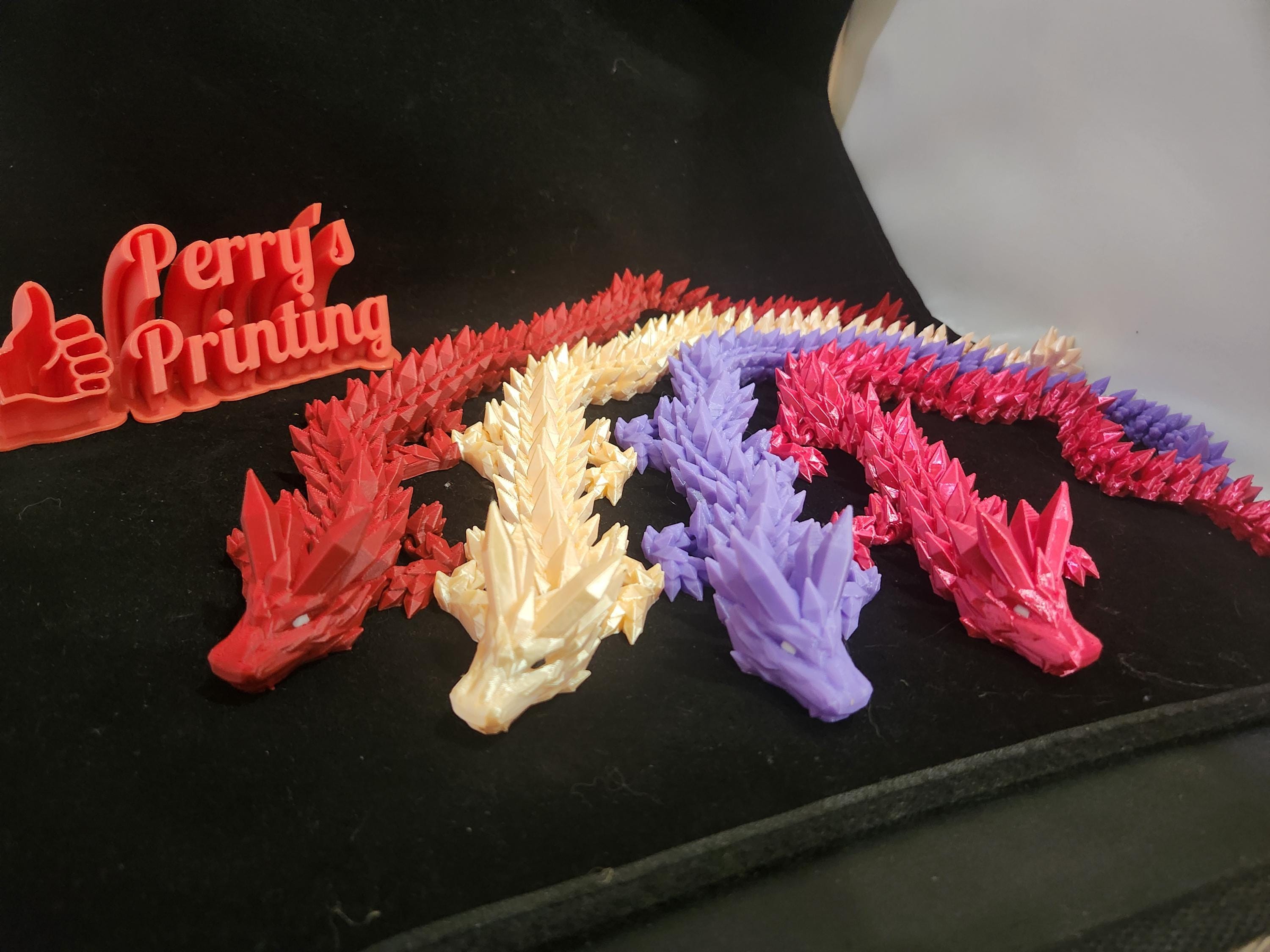 Colorful 3D printed articulated dragons on black fabric with a Perry's Printing sign