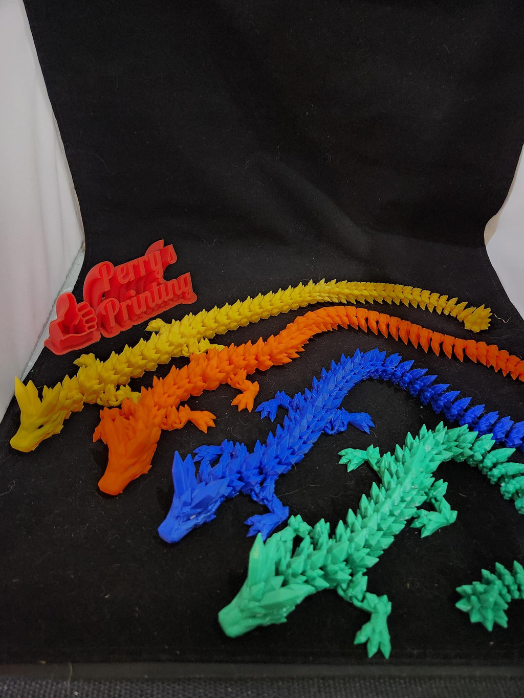 Colorful 3D printed articulated dragon models in yellow, orange, blue, and green on black backdrop