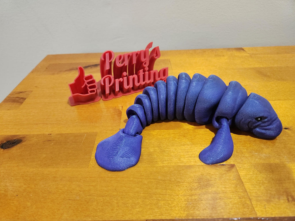 3D printed blue manatee figurine and red Perry's Printing sign on wooden table