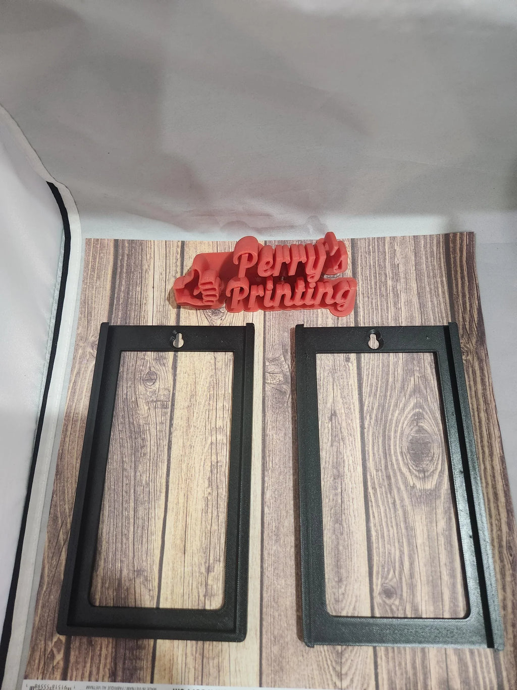 Two black rectangular 3D printed frames and a red Perry's Printing logo on wood background