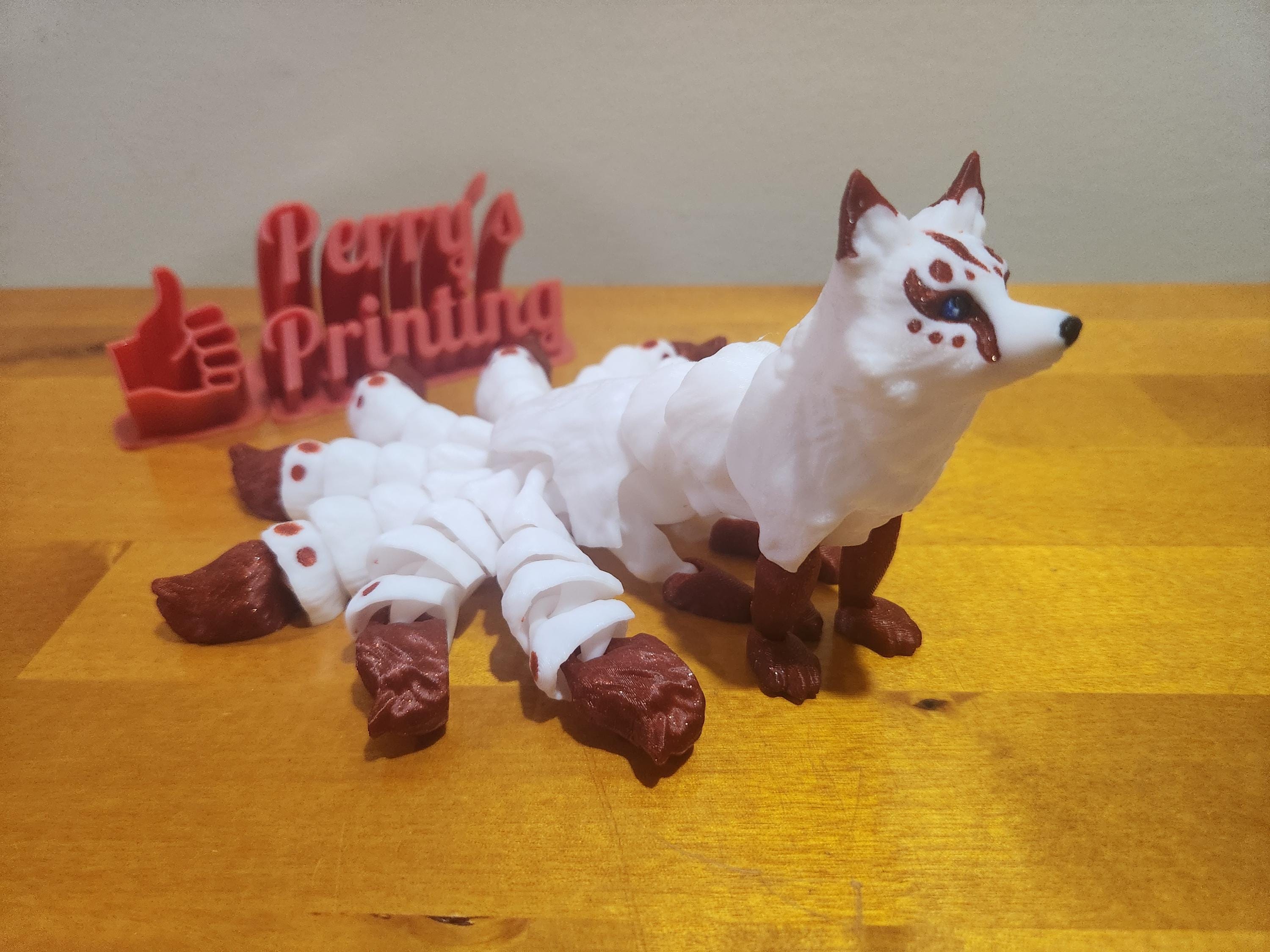3D printed white and brown fox figurine with multiple tails on a wooden surface