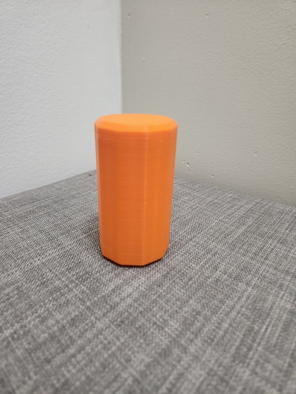 Orange 3D printed polygonal container on a gray fabric surface