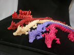 Colorful 3D printed articulated dragon models and a red Perry's Printing sign on black fabric