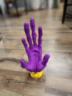 Purple 3D printed hand sculpture on gold base, displayed on wood floor