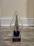 Custom glass award with swirl design and engraved plaque on wooden floor, ideal for recognition and appreciation.