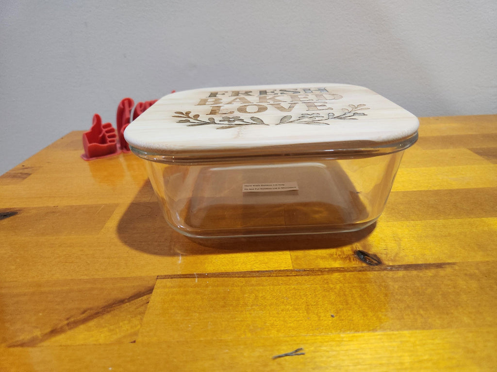 Glass baking dish with engraved wooden lid reading 'Fresh Baked Love' on wooden table
