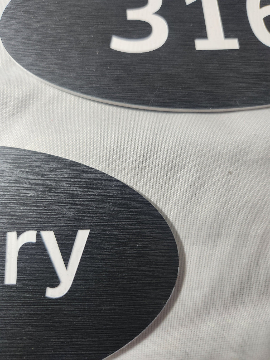 Close-up of black laser engraved oval signs with white text on a fabric surface