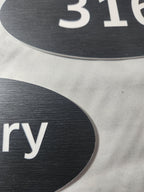 Close-up of black laser engraved oval signs with white text on a fabric surface