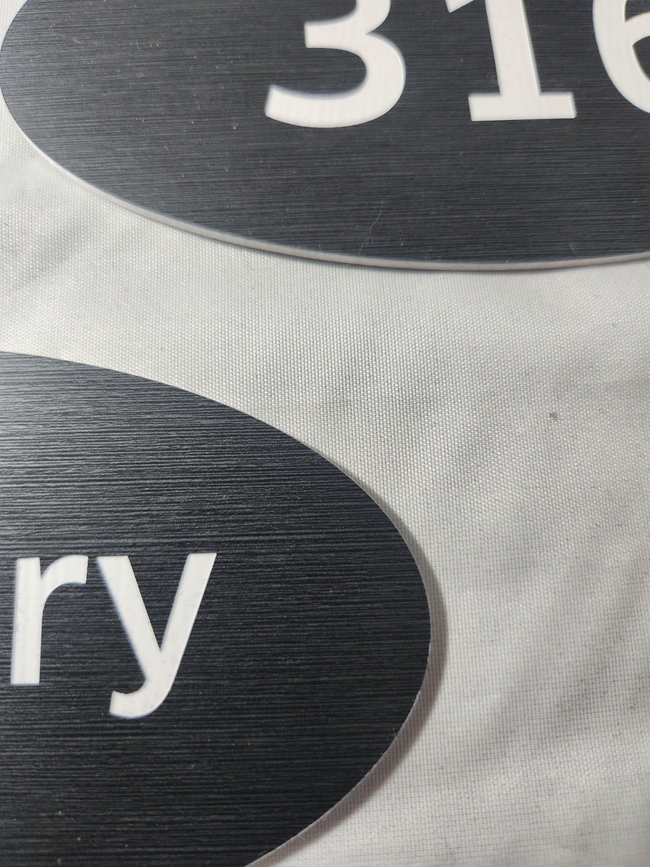 Close-up of black laser engraved oval signs with white text on a fabric surface