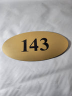 Oval gold metal door number plaque with black 143 on white background