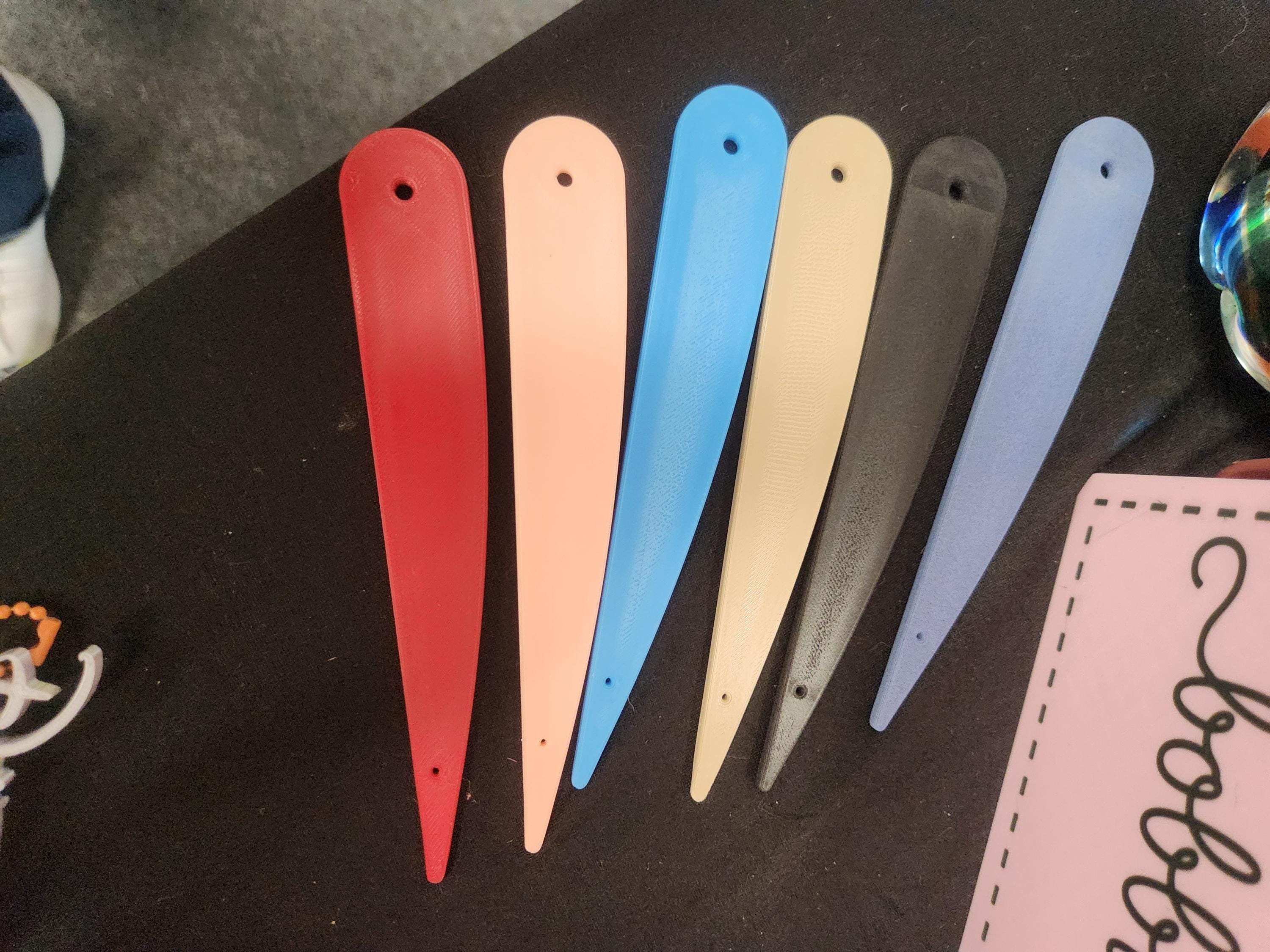 Six colorful 3D printed plastic fan blades with holes, displayed on a dark surface