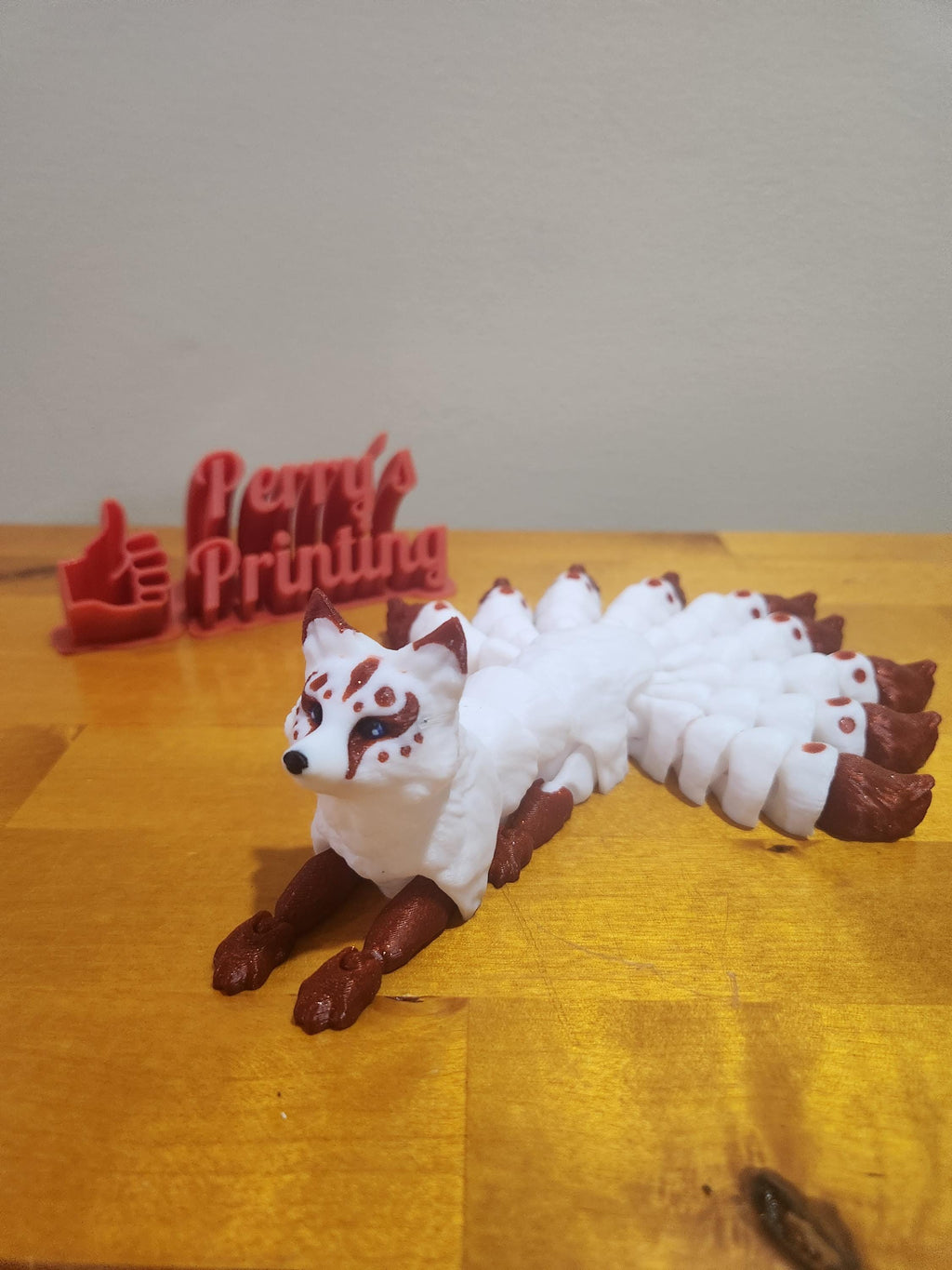 3D printed white and red nine-tailed fox figurine with engraved business sign on wooden table