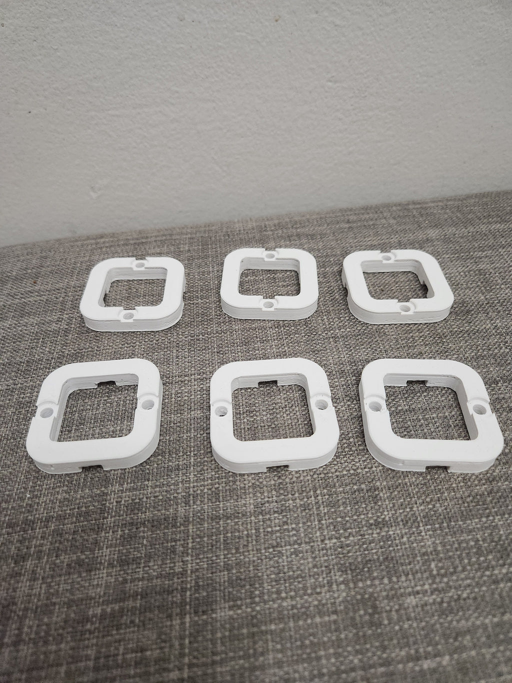 Set of six white 3D printed plastic square mounting brackets on a gray fabric surface