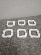 Set of six white 3D printed plastic square mounting brackets on a gray fabric surface