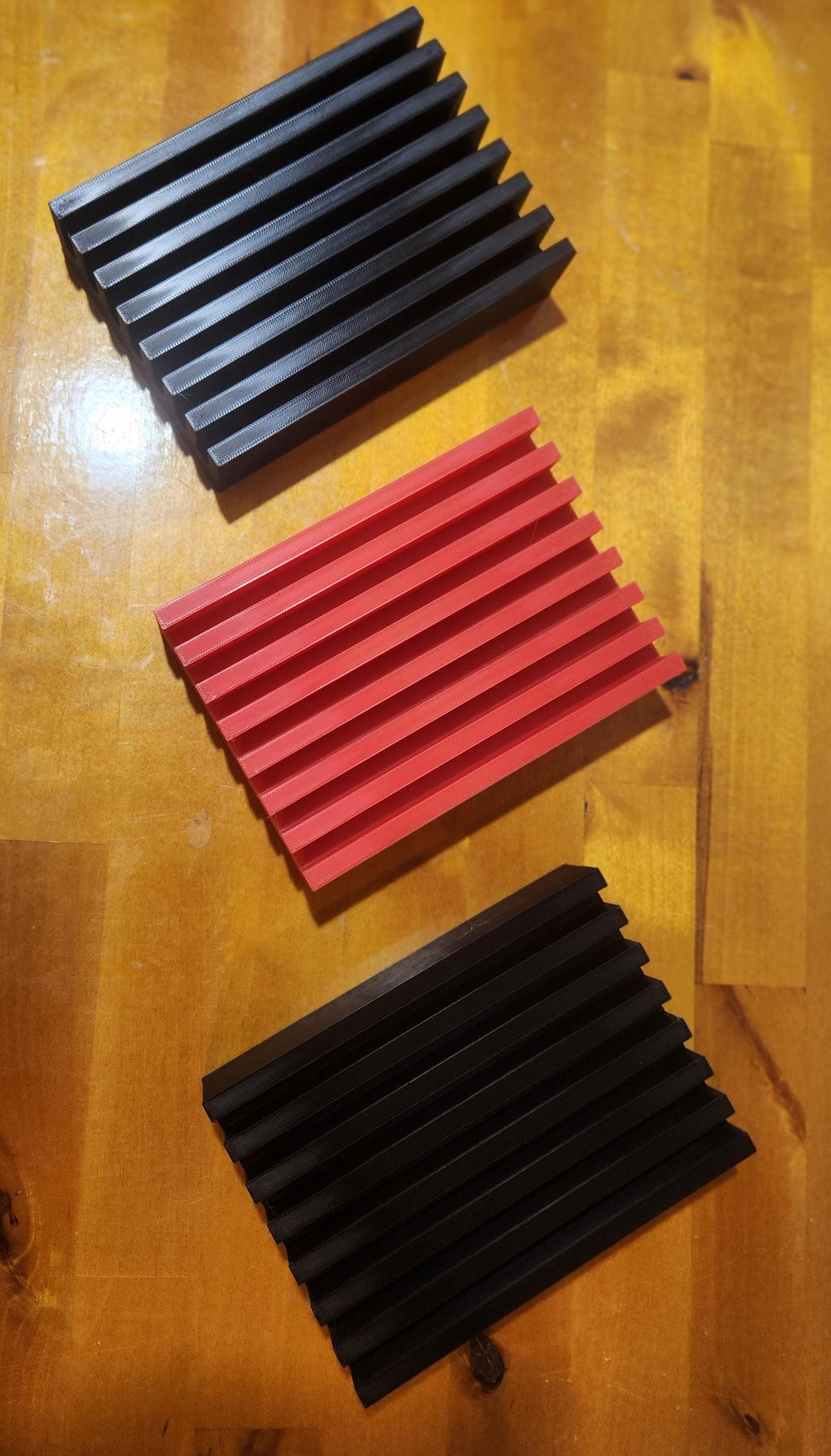 Three rectangular 3D printed slotted organizers in black and red on a wood surface