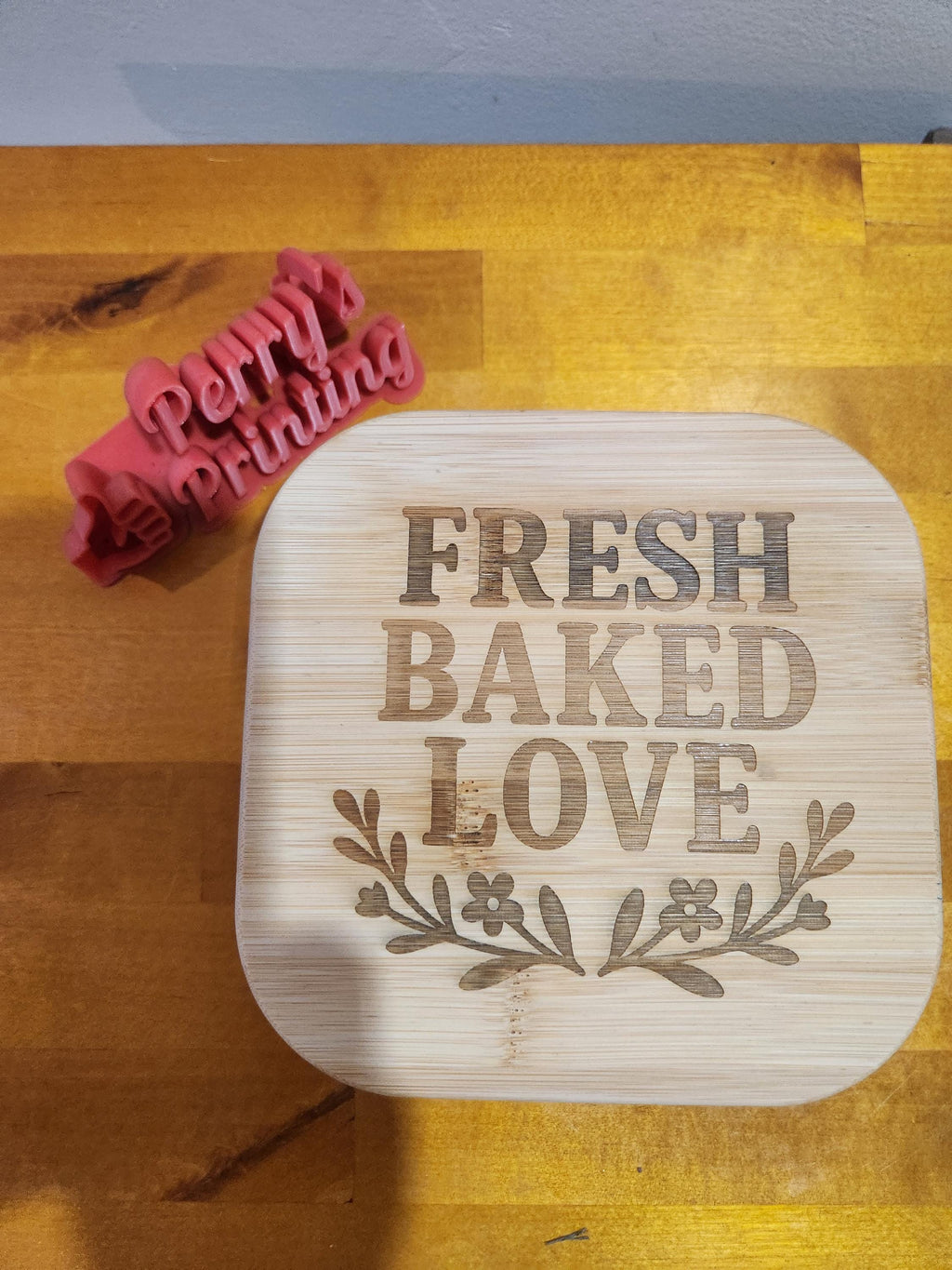 Laser engraved bamboo lid with 'Fresh Baked Love' and a 3D printed baking cookie cutter