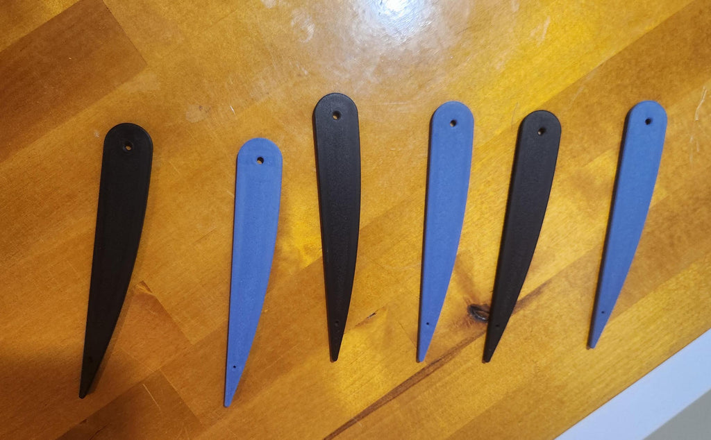 Six 3D printed blue and black pointed tags with holes, arranged on a wooden surface.