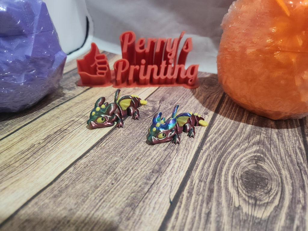 Colorful 3D printed dragons on wood surface with engraved Perry's Printing sign in background