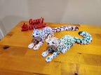3D printed articulated leopard figurines with colorful spots on a wooden table