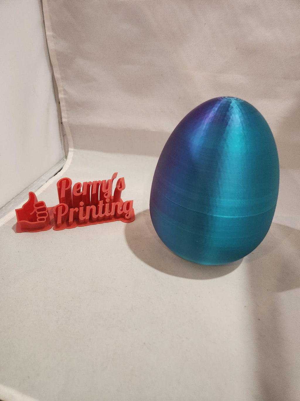 Blue 3D printed egg and red 3D printed Perry's Printing sign on white background