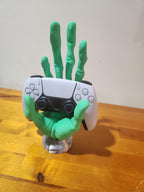 Green 3D printed skeleton hand holding a white gaming controller on a wooden surface