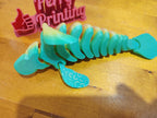 Articulated 3D printed green sea creature toy on wood surface, laser-cut sign in background