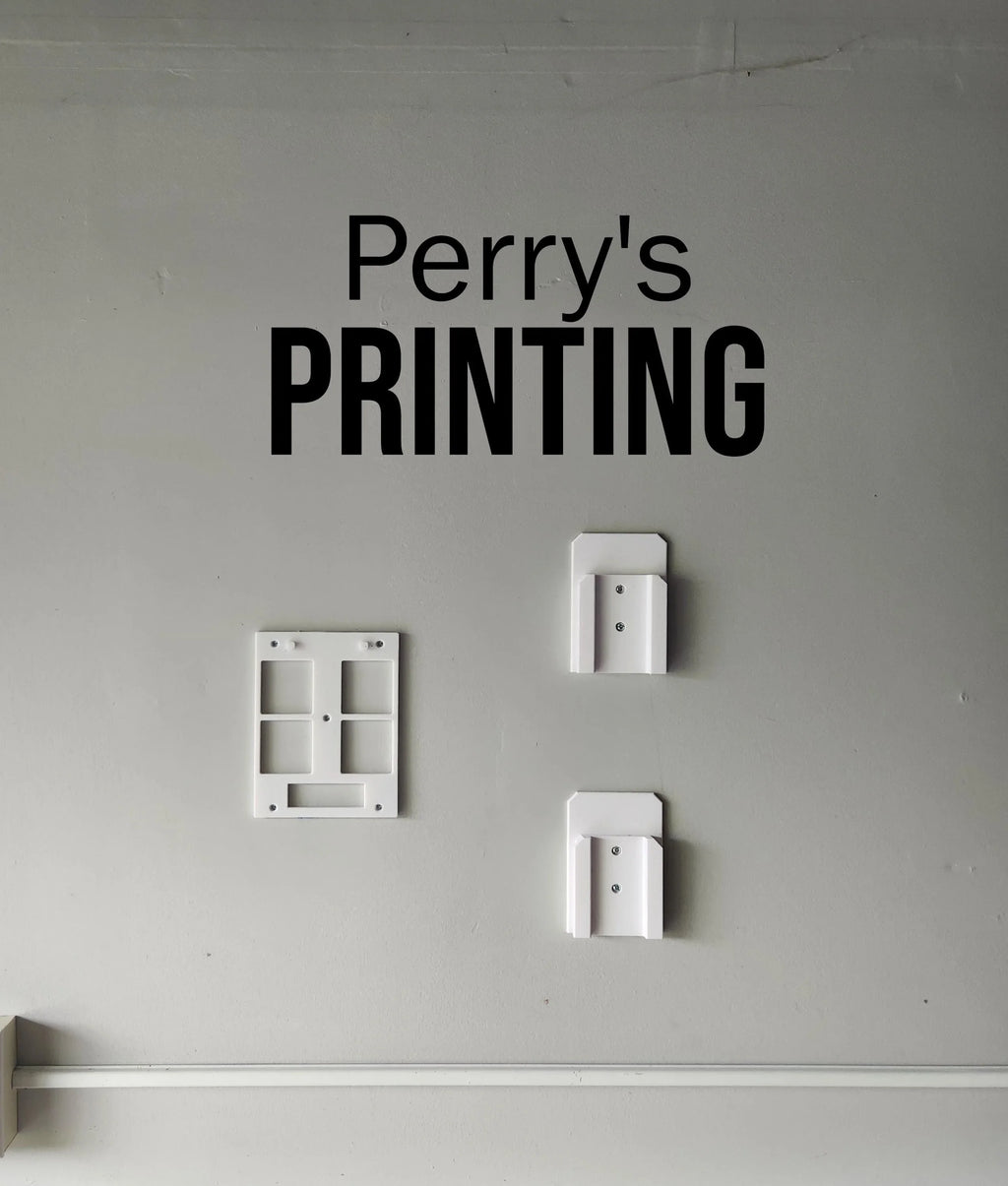Wall-mounted 3D printed holders and frames on a gray wall below bold Printing sign