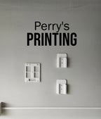 Wall-mounted 3D printed holders and frames on a gray wall below bold Printing sign