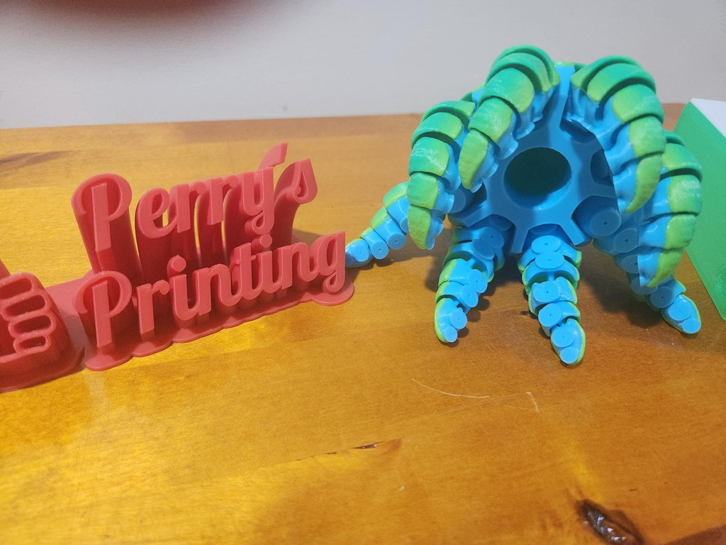 3D printed red Perry's Printing sign and blue-green articulated toy on wood surface
