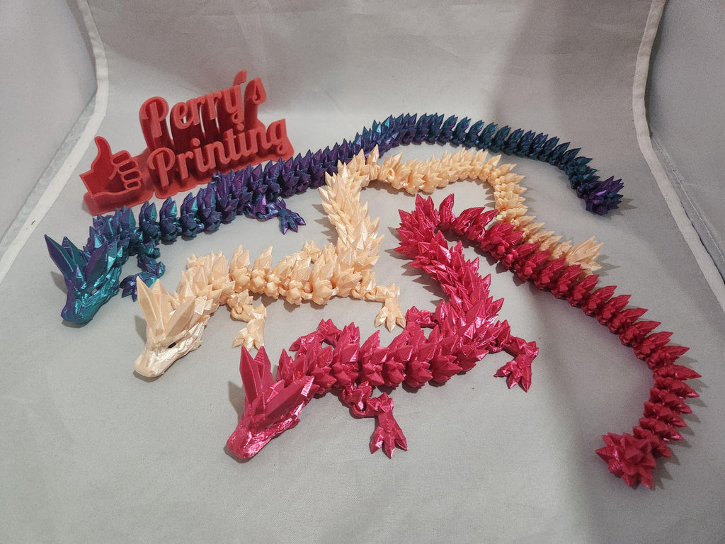 Colorful 3D printed dragon figurines in blue, cream, and red with a red printed display sign.
