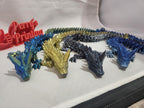 3D printed articulated dragon figurines in metallic blue, gold, and black on white background