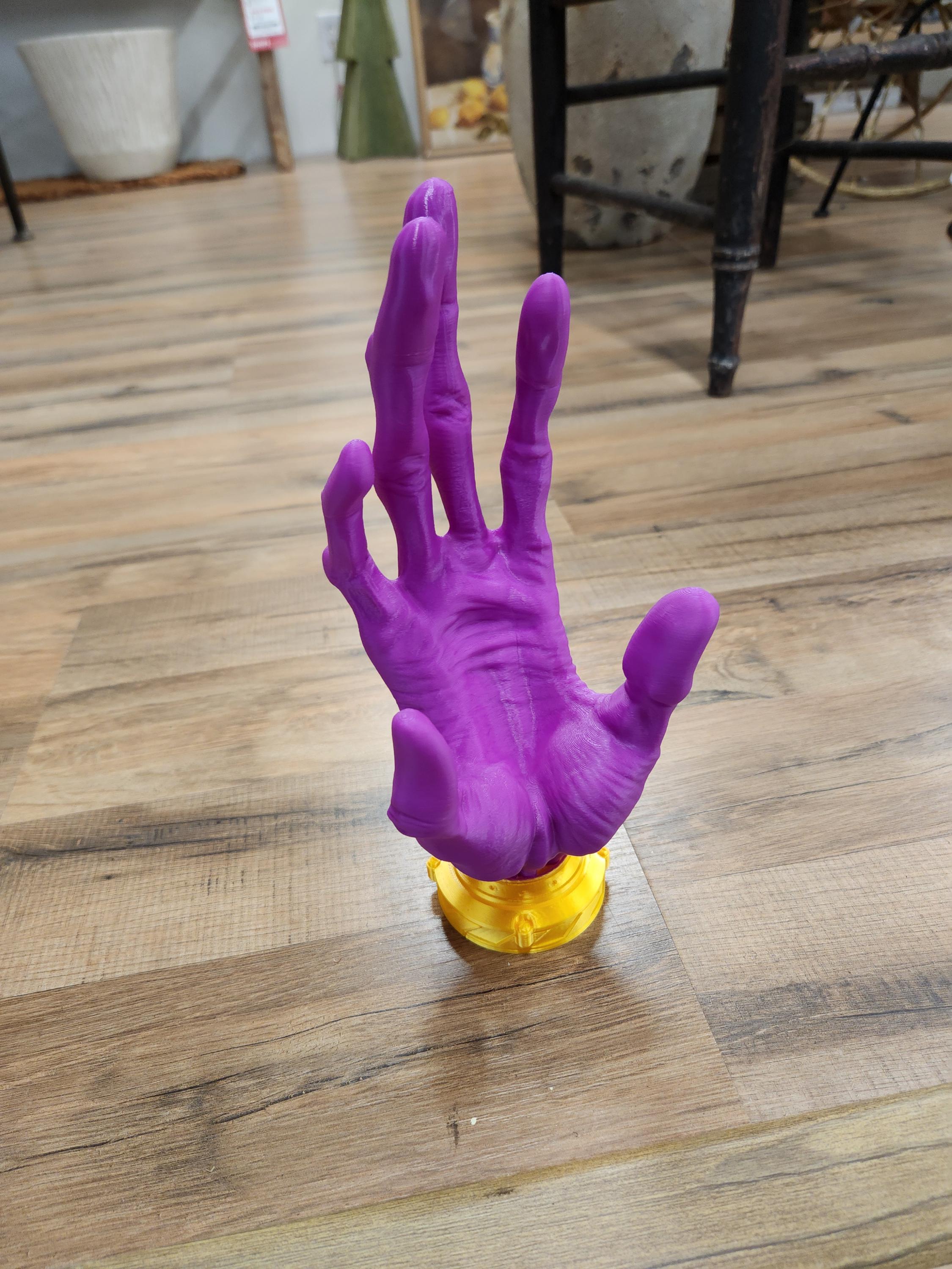 Purple 3D printed hand sculpture with gold base on wood floor, detailed engraving