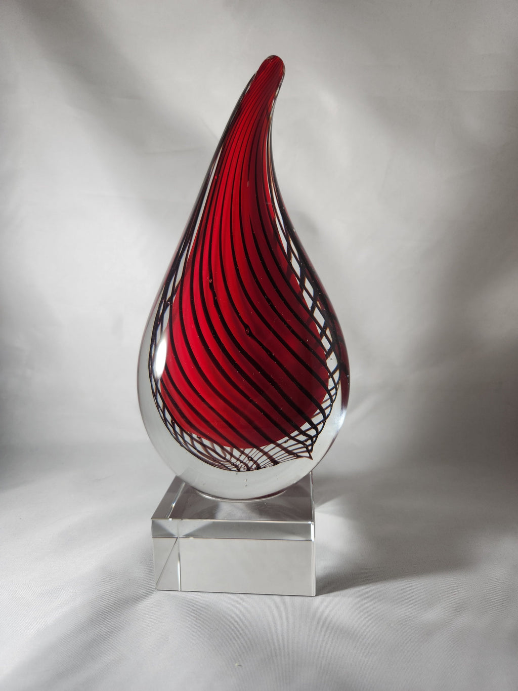 Red and clear glass art award with swirl pattern on a transparent base, against white backdrop
