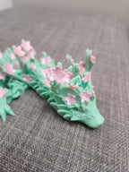 Mint green 3D printed dragon with pink cherry blossom flowers on a gray fabric surface