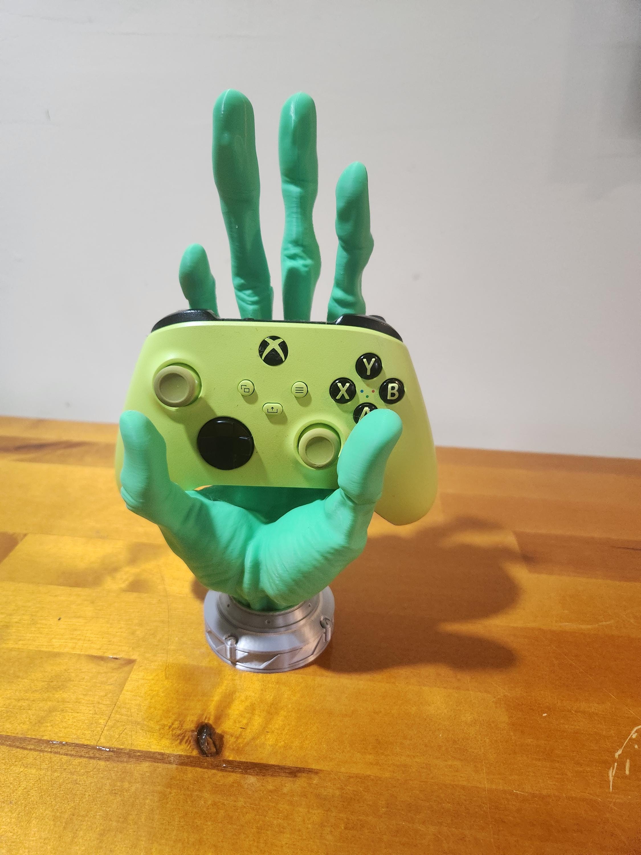 3D printed green alien hand holding an Xbox controller on a wooden table