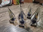Four glass teardrop-shaped custom awards with colorful swirls on a wooden floor