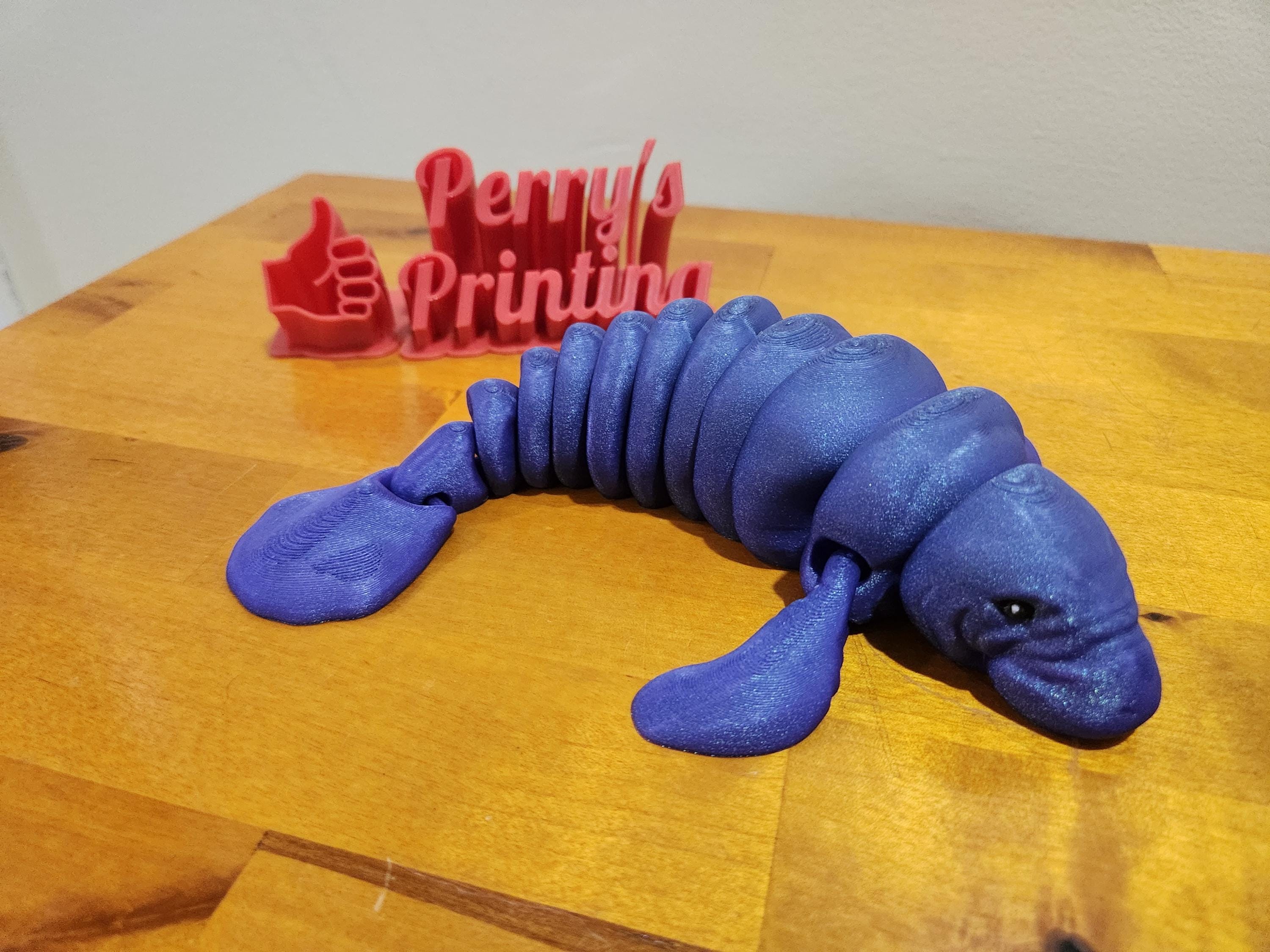 Articulated blue 3D printed manatee toy on wooden table, red sign in background