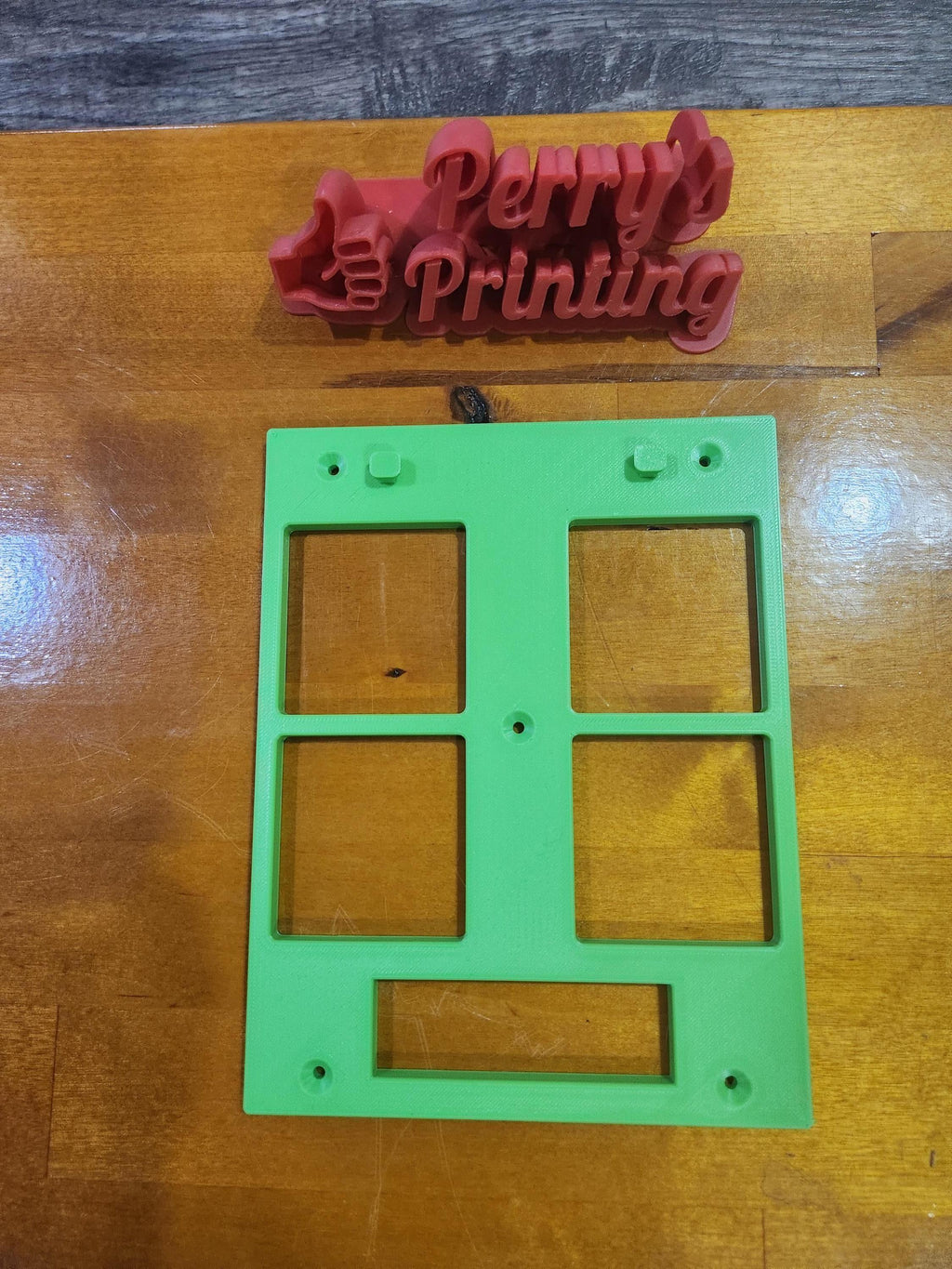 3D printed red logo with thumbs up and text, green plastic sign frame on wood surface